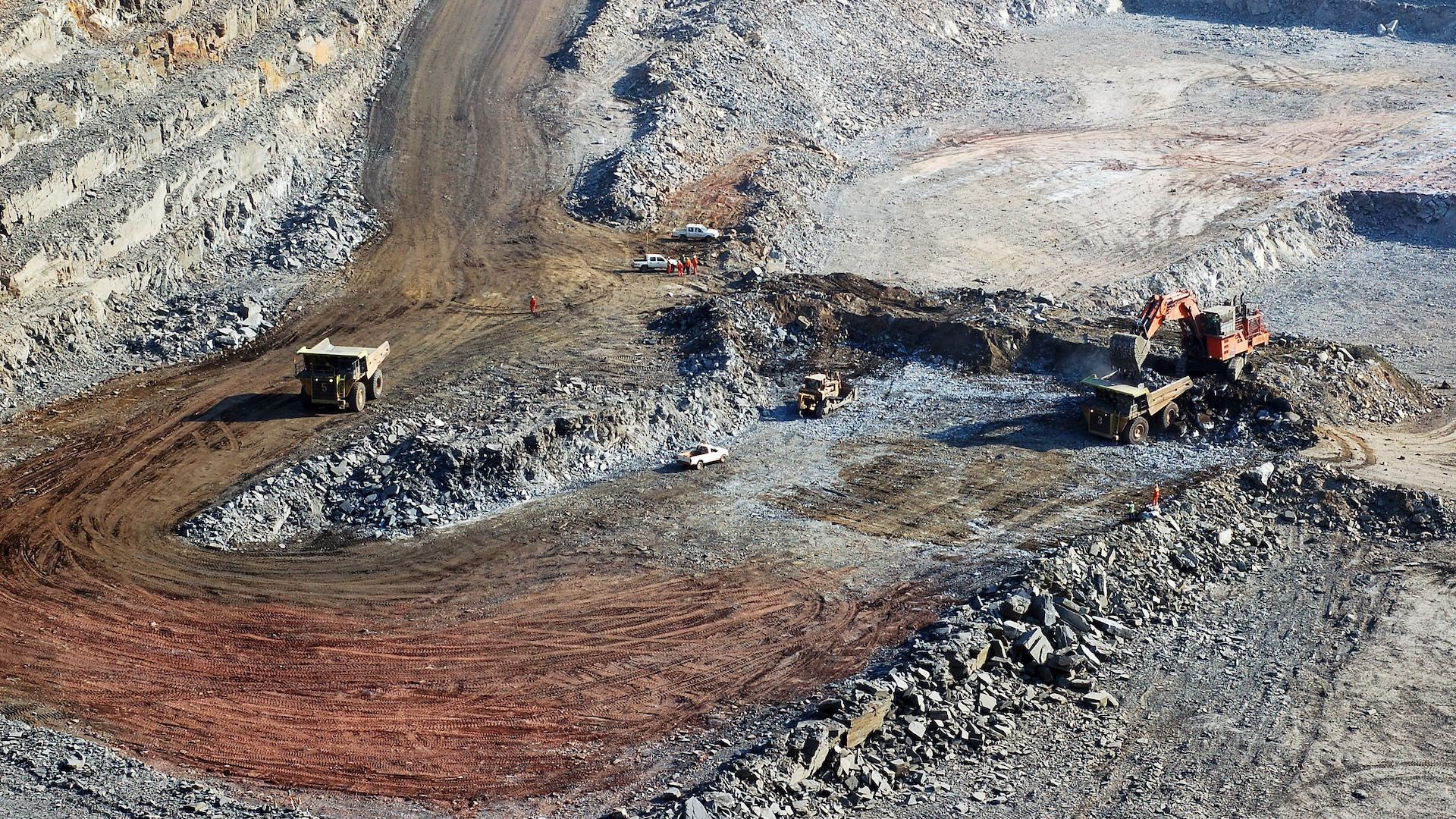 A pair of 100-tonne haul trucks work on the floor of an open-pit copper mine. A large excavator (digger) and bulldozer also work to remove ore from the pit - 1920x1080.jpg